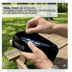 A person outdoors holding open a black zippered pouch with the brand name BREEZY on the side. The pouch contains blue cylindrical items, and the background shows a wooden picnic table and green grass with a text overlay at the top. 