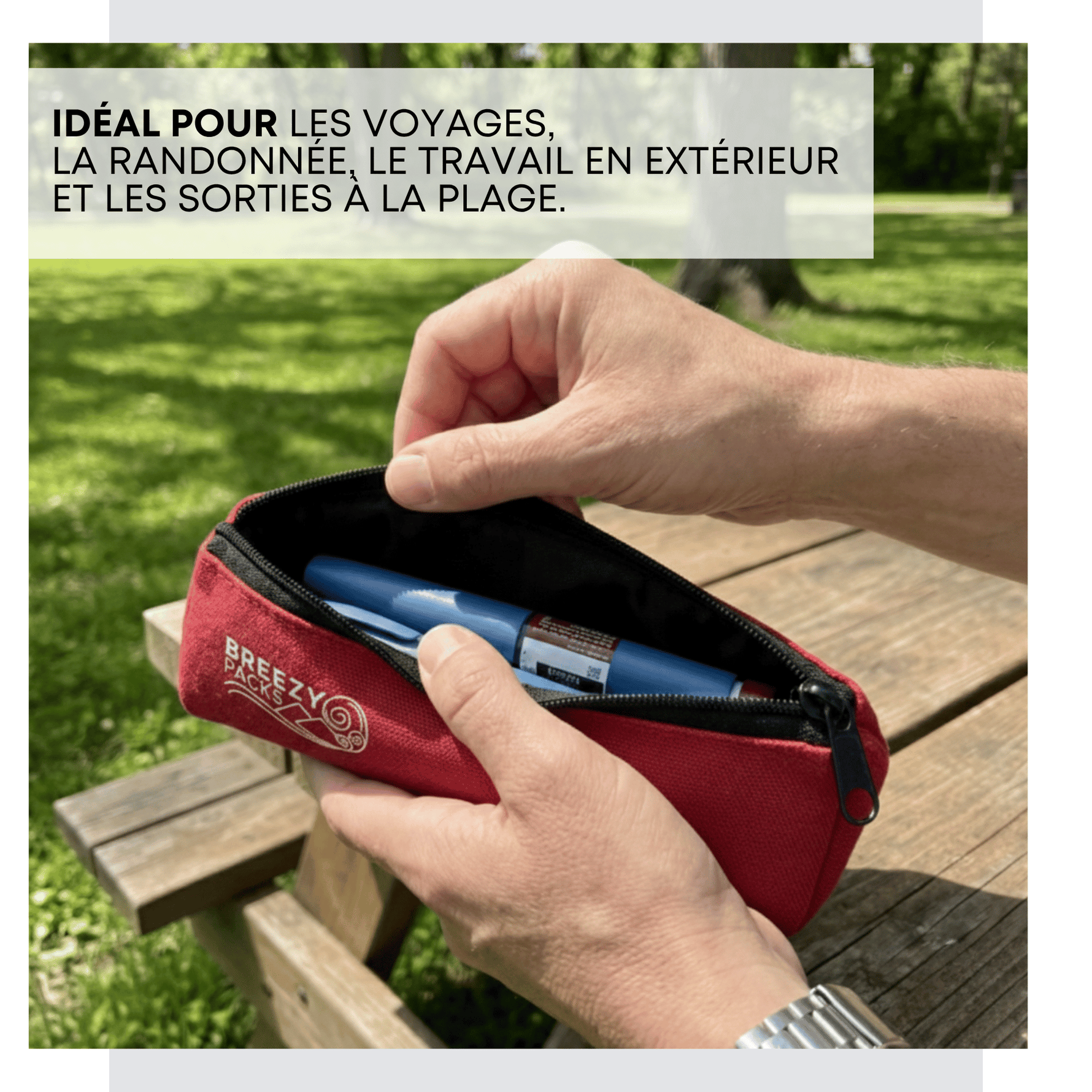 A red zippered pouch with a white 'BREEZY Packs' logo, held open by two hands over a wooden park bench with green grass in the background. A white text box at the top reads 'IDÉAL POUR LES VOYAGES, LA RANDONNÉE, LE TRAVAIL EN EXTÉRIEUR ET LES SORTIES À LA PLAGE.
